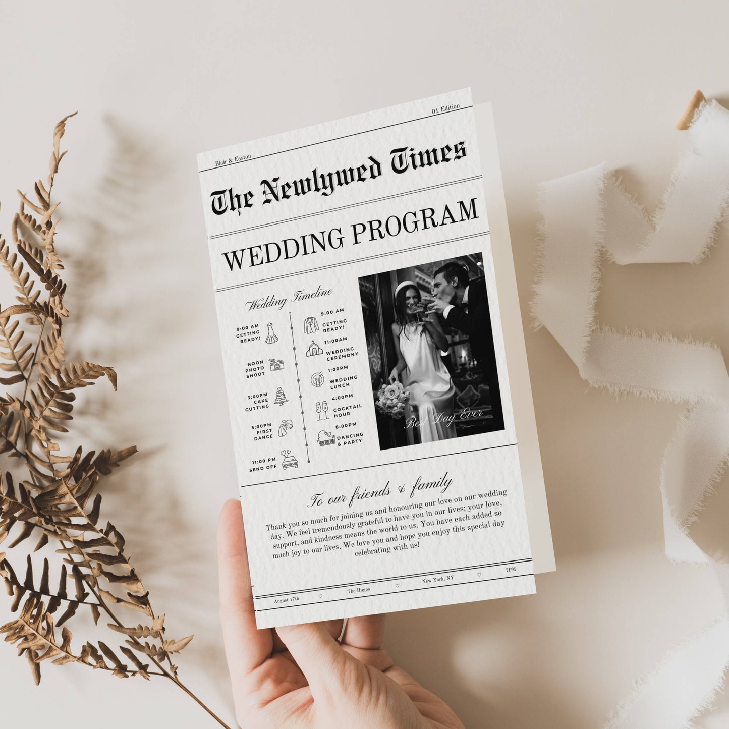 Wedding program from 'The Newlywed Times' held by a hand with dried leaves on a light background