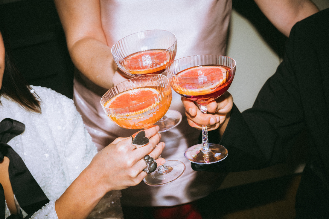 guests dressed in holiday cocktail dress attire with festive holiday drinks in hand cheersing each other