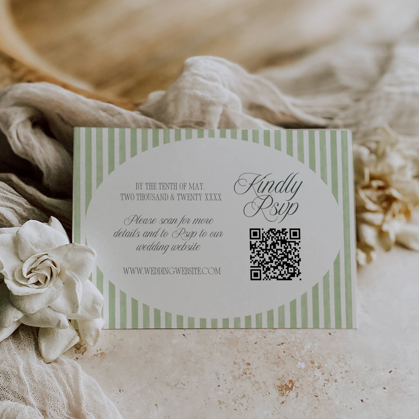 Wedding invitation card with QR code on a textured surface with flowers and fabric.