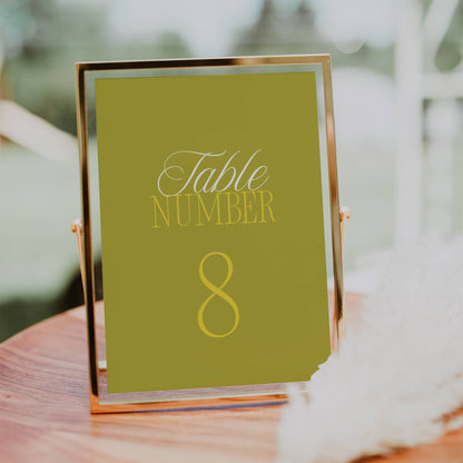 Table number 8 sign on a green background with gold text, placed on a wooden surface outdoors.
