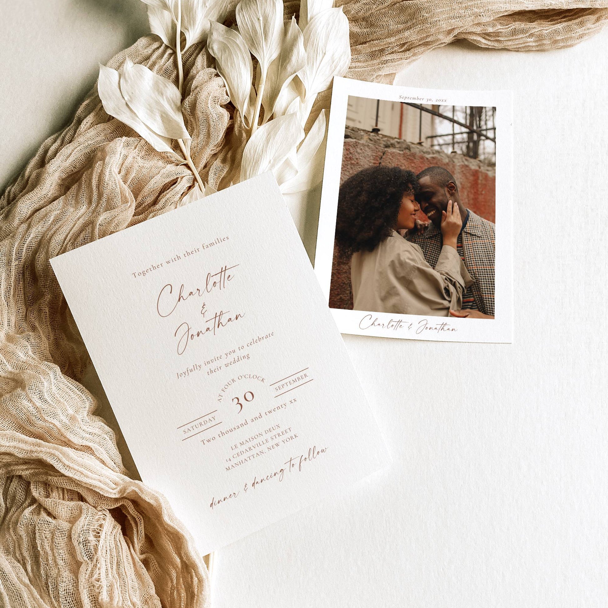 Invitation card with a photo of a couple embracing, surrounded by beige fabric and dried flowers on a light background.