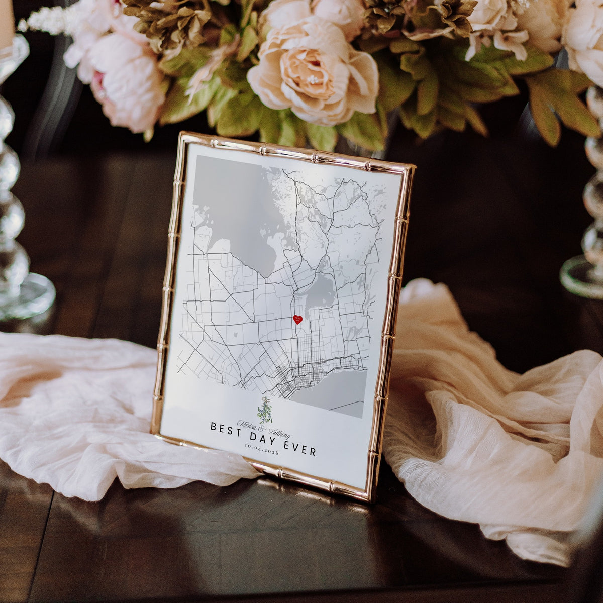 Custom wedding map print with mistletoe in a gold bamboo frame on a table with blush roses and silk runner