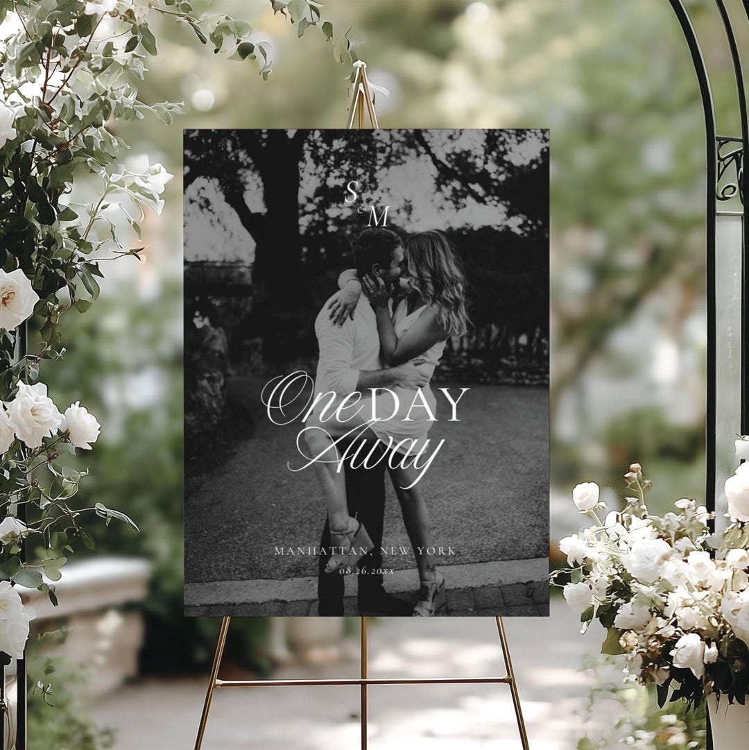 Black and white photo rehearsal welcome sign on a gold metal easel with a couple embracing photo, One Day Away script text, outdoor styling