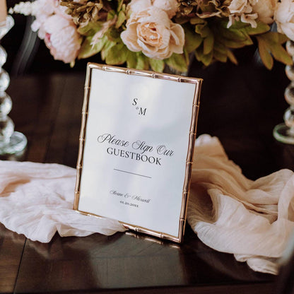 Old Money monogram wedding guestbook sign in a gold bamboo-style frame, styled on a dark wood surface