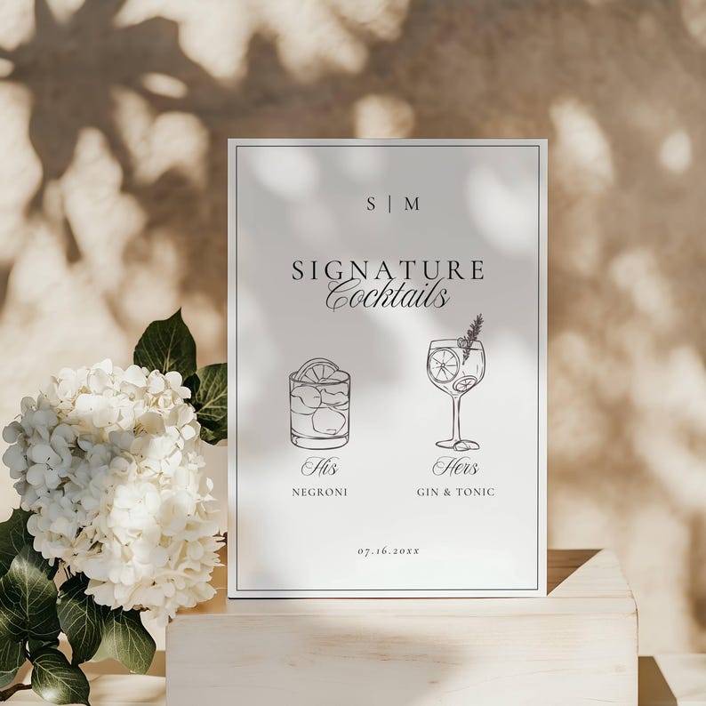 Signature cocktails sign with monogram initials and wedding date styled on a wooden surface with florals