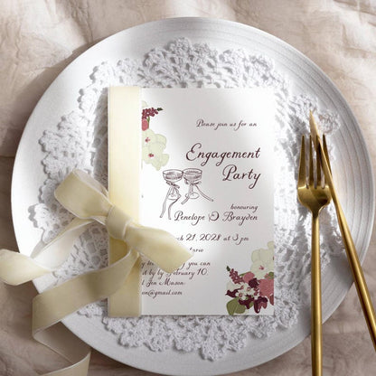Plum floral engagement invitation styled on a white plate with lace doily, gold flatware, and cream ribbon