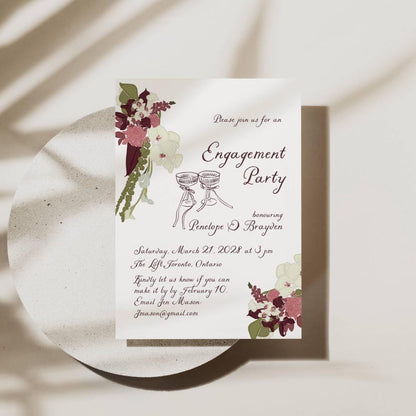 Plum floral engagement invitation styled with champagne flutes and floral arrangements