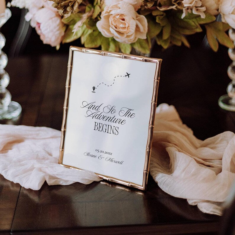 And So The Adventure Begins wedding sign displayed in a gold bamboo-style frame