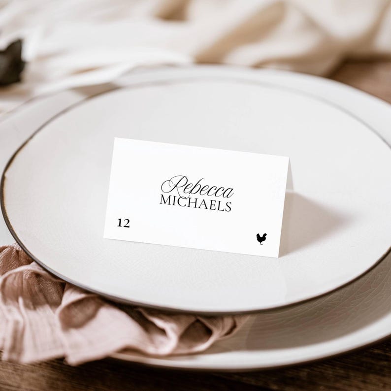 Old Money place card with guest number 12, script name, and rooster meal icon, set on a dark-rimmed plate with a folded napkin