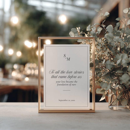 Love Stories Before Ours sign in gold frame on table with greenery