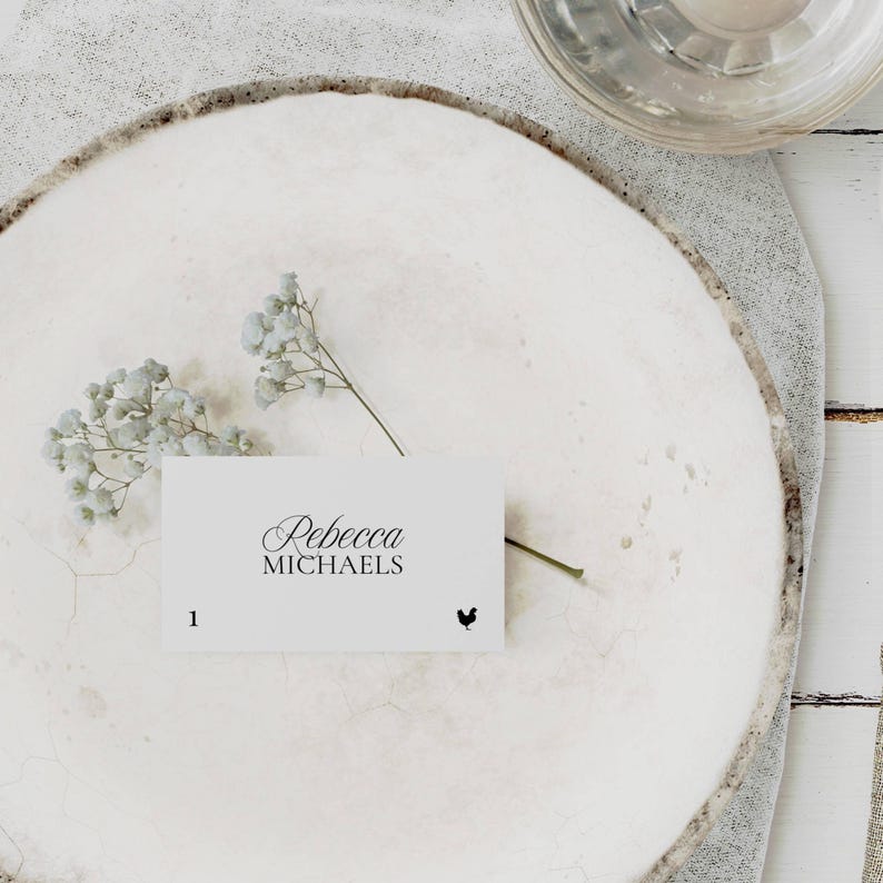 Old Money place card with elegant script name and hand-drawn chicken meal icon, resting on a textured plate with light blue florals