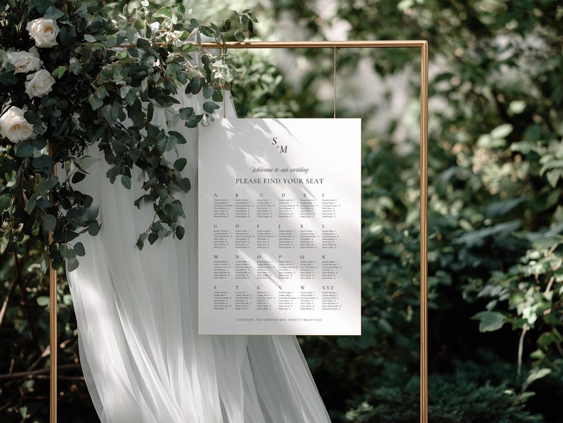 Seating chart displayed on a gold frame stand with flowing white tulle and greenery