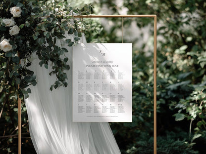 Seating chart displayed on a gold frame stand with flowing white tulle and greenery