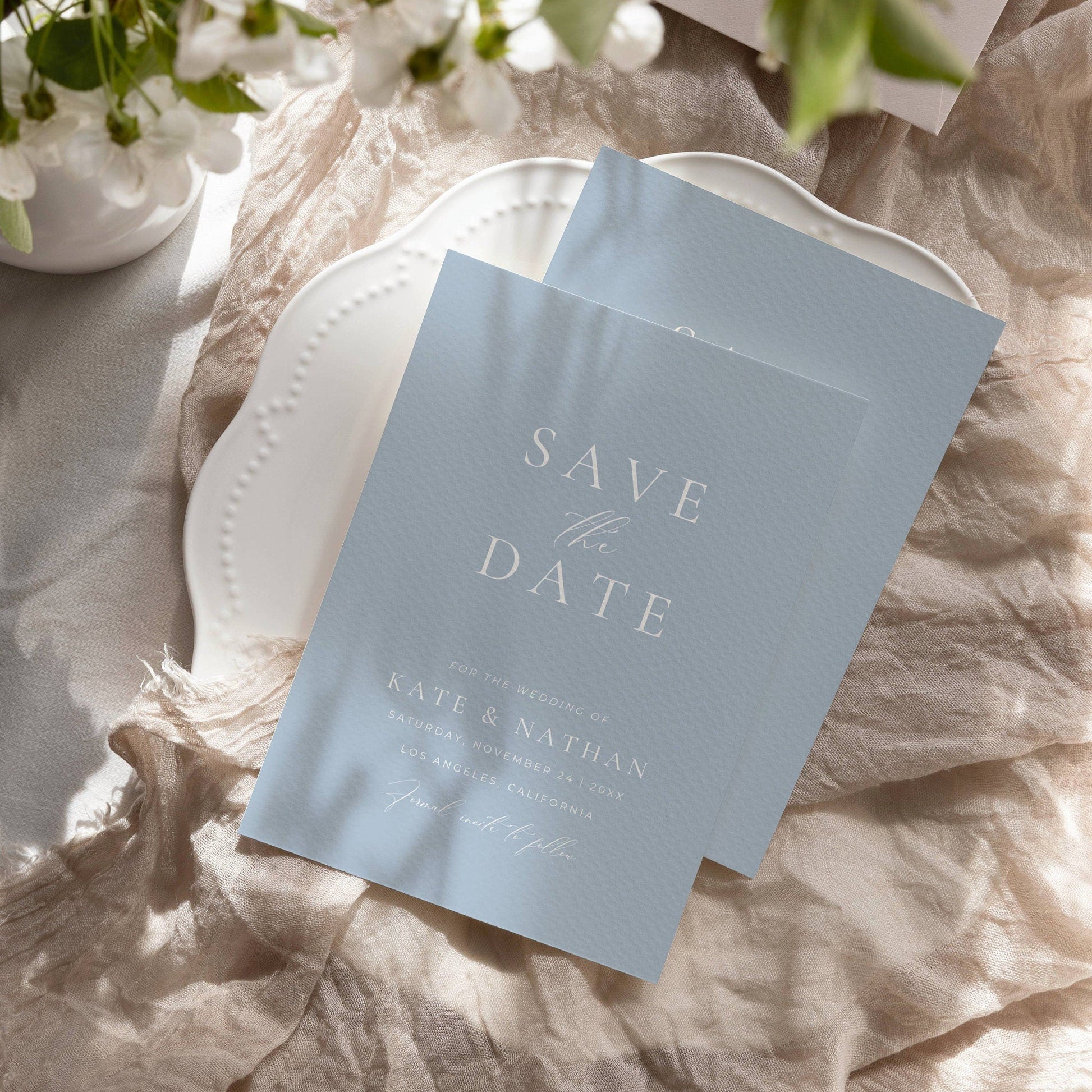 dusty blue save the date invitation on a plate with soft shadow