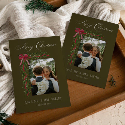 Two olive green mistletoe Merry Christmas wedding photo cards on a wooden tray with white gauze and pine sprigs