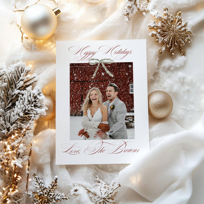 First Christmas married photo card with deep red calligraphy and bow, framed by gold baubles and snowflakes
