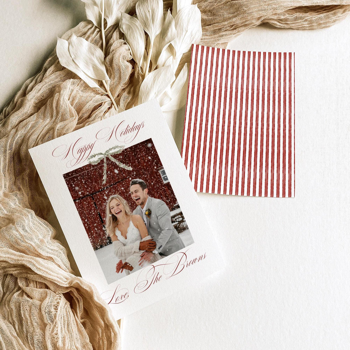 Double-sided 5x7 newlywed holiday card with red ribbon bow and striped back styled with dried white leaves