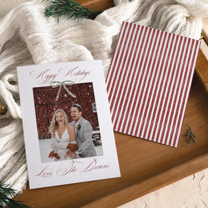 Front and red stripe back of the Happy Holidays wedding photo card on a wooden tray with a knit throw and rosemary sprig
