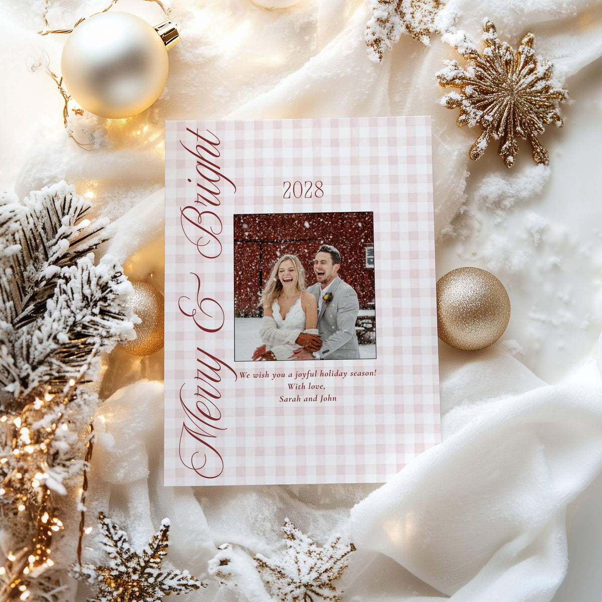 Gingham newlywed holiday card with burgundy script framed by gold ornaments, snowflakes and frosted fir branches