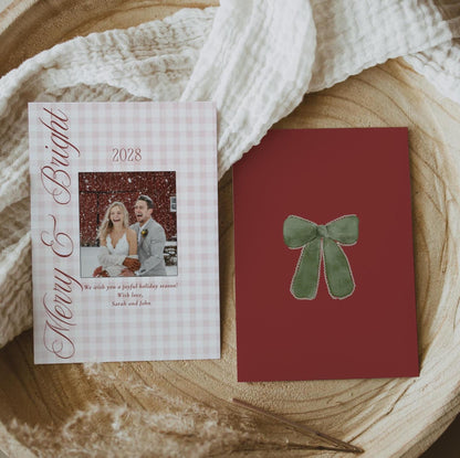 Front and burgundy back of the gingham Merry and Bright wedding photo card on a round wood slice with linen and dried grass