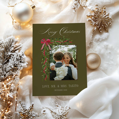 Olive green first Christmas married photo card surrounded by gold snowflake ornaments and frosted branches