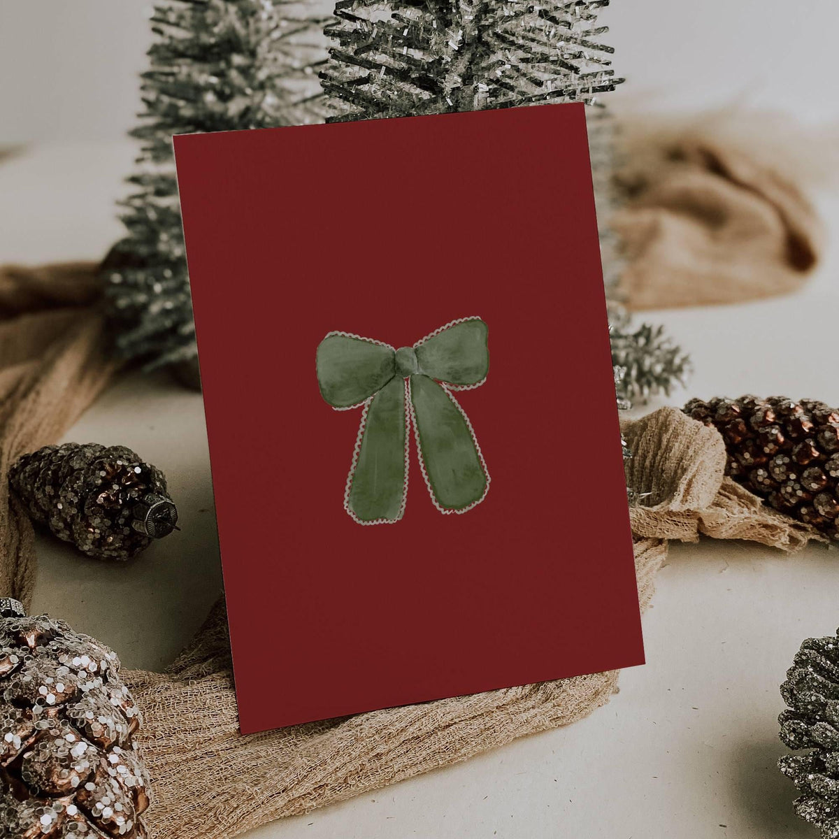 Burgundy card back with a hand-painted green velvet bow, styled with frosted pinecones and silver Christmas trees