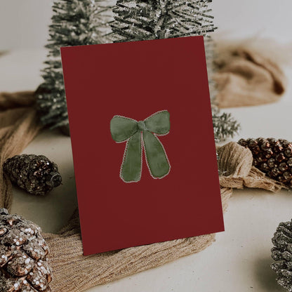 Burgundy card back with a hand-painted green velvet bow, styled with frosted pinecones and silver Christmas trees